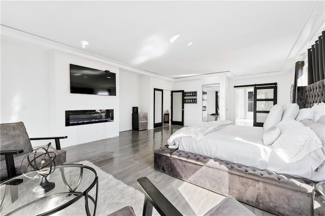 bedroom featuring a glass covered fireplace, wood finished floors, and ornamental molding