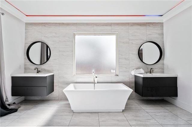 bathroom featuring a freestanding tub, tile walls, two vanities, and a sink