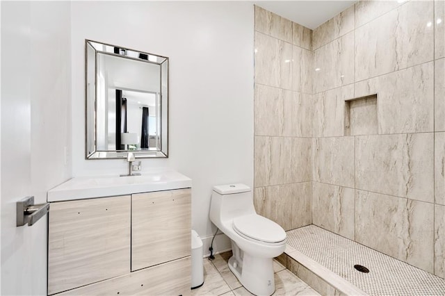 bathroom featuring tiled shower, toilet, marble finish floor, and vanity