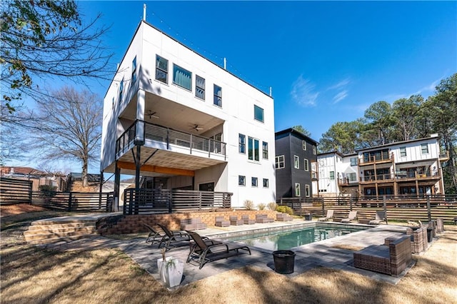 rear view of property with fence, stucco siding, a balcony, a patio area, and a ceiling fan