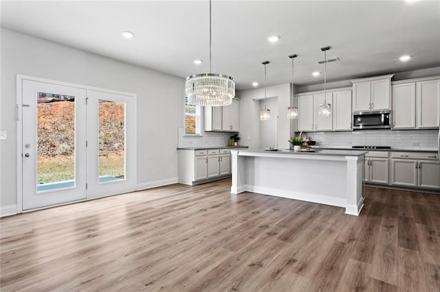 kitchen featuring stainless steel microwave, backsplash, visible vents, decorative light fixtures, and wood finished floors