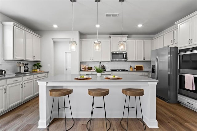 kitchen with a breakfast bar area, wood finished floors, visible vents, and appliances with stainless steel finishes