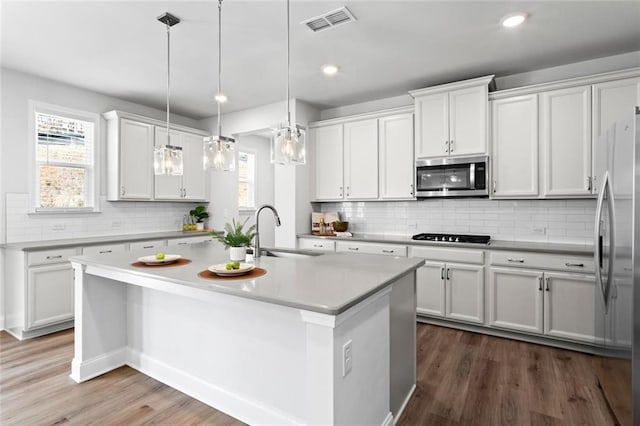 kitchen with visible vents, an island with sink, a sink, stainless steel appliances, and white cabinets