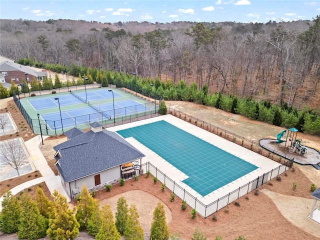 view of swimming pool featuring fence, a tennis court, and a wooded view