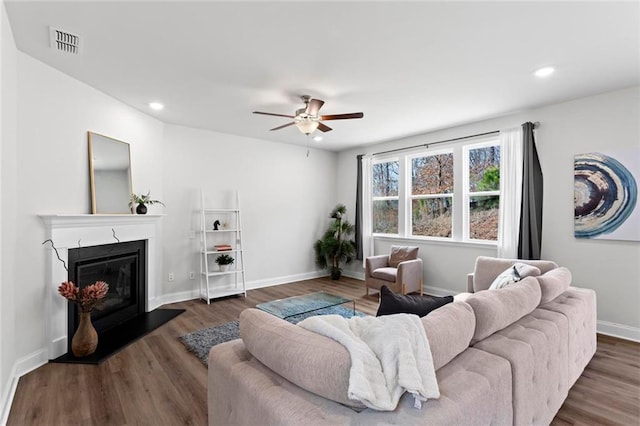 living area with visible vents, a glass covered fireplace, wood finished floors, baseboards, and ceiling fan