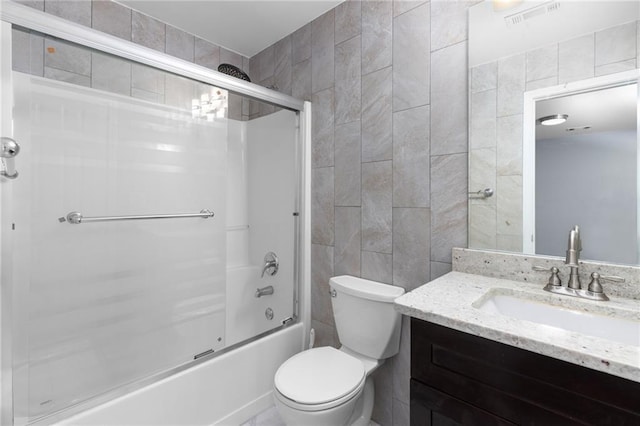 full bathroom featuring toilet, bath / shower combo with glass door, tile walls, and vanity