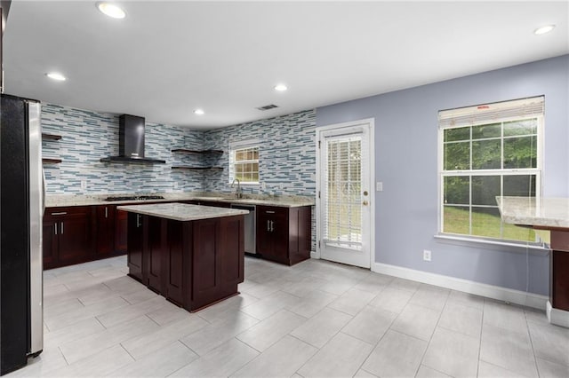 kitchen featuring a center island, wall chimney exhaust hood, stainless steel appliances, backsplash, and dark brown cabinets