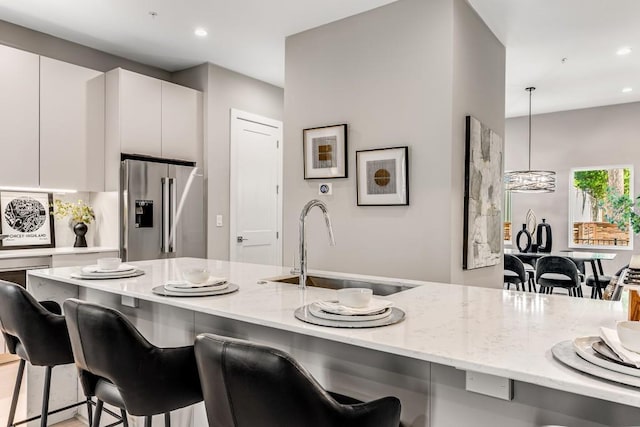 kitchen featuring pendant lighting, white cabinets, a kitchen breakfast bar, high quality fridge, and sink