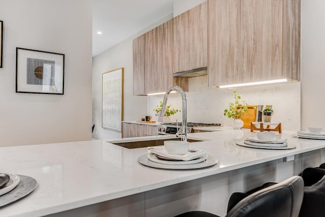 kitchen featuring light stone countertops, a breakfast bar area, and light brown cabinets