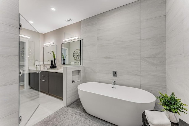 bathroom with tile walls, vanity, a bathtub, and tile patterned flooring