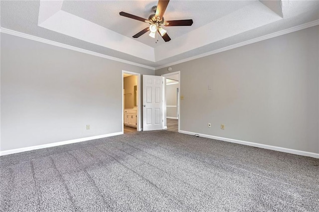 unfurnished bedroom featuring ornamental molding, a tray ceiling, dark carpet, and ceiling fan