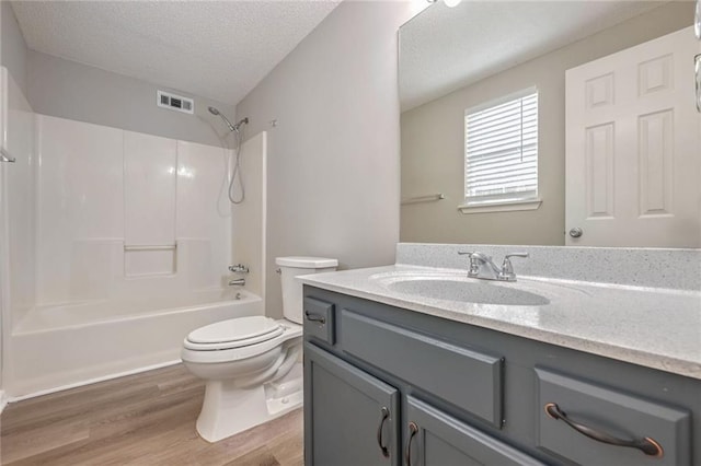 full bathroom featuring wood-type flooring, vanity, a textured ceiling, shower / washtub combination, and toilet