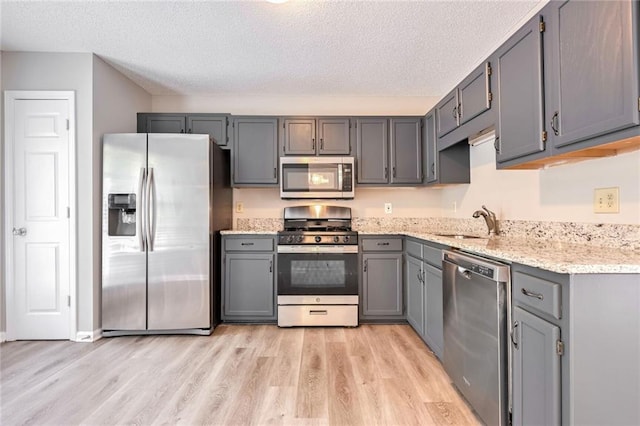 kitchen with gray cabinets, a textured ceiling, light hardwood / wood-style floors, and appliances with stainless steel finishes