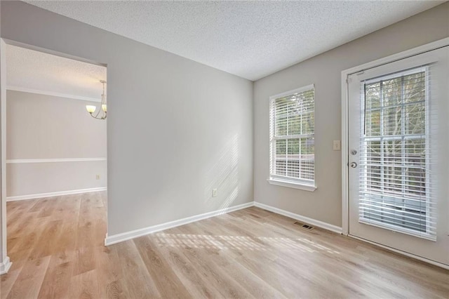 empty room featuring a textured ceiling, light hardwood / wood-style floors, a healthy amount of sunlight, and a chandelier