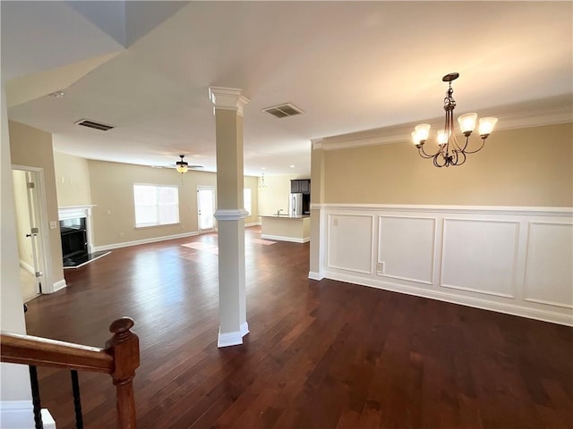 empty room with ceiling fan with notable chandelier, dark wood-type flooring, a premium fireplace, visible vents, and ornate columns