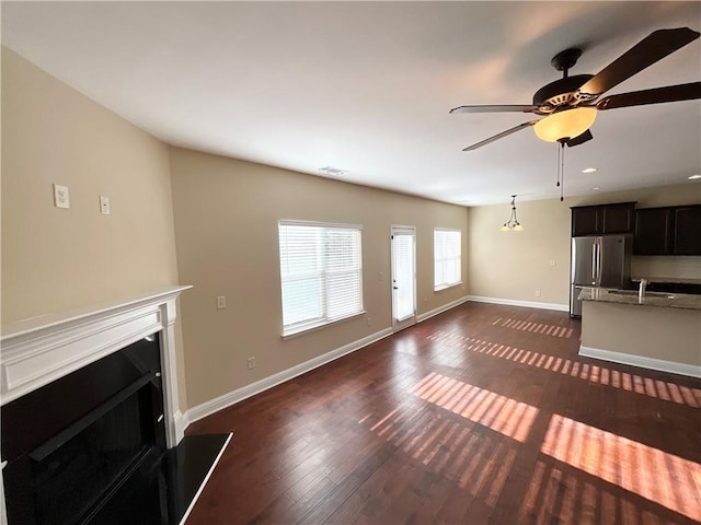 unfurnished living room featuring dark wood-style floors, a fireplace, a sink, ceiling fan, and baseboards