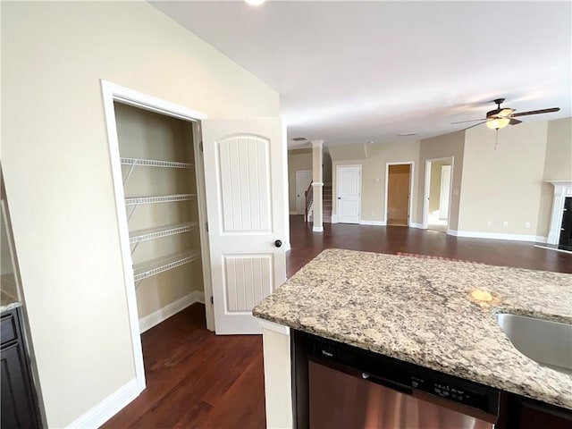 kitchen with a fireplace, dark wood finished floors, stainless steel dishwasher, a ceiling fan, and light stone countertops