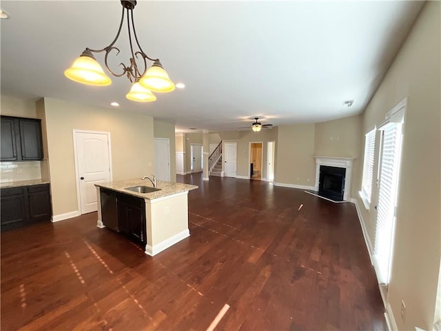 kitchen featuring baseboards, decorative backsplash, dark wood-style floors, a fireplace, and a sink