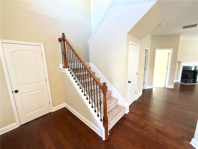 stairway featuring visible vents, a fireplace, baseboards, and wood finished floors