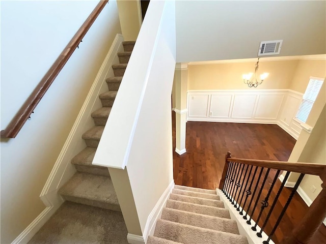 stairway with a decorative wall, wood finished floors, visible vents, wainscoting, and an inviting chandelier