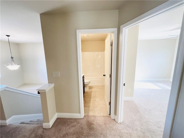 hall with light carpet, baseboards, and an upstairs landing