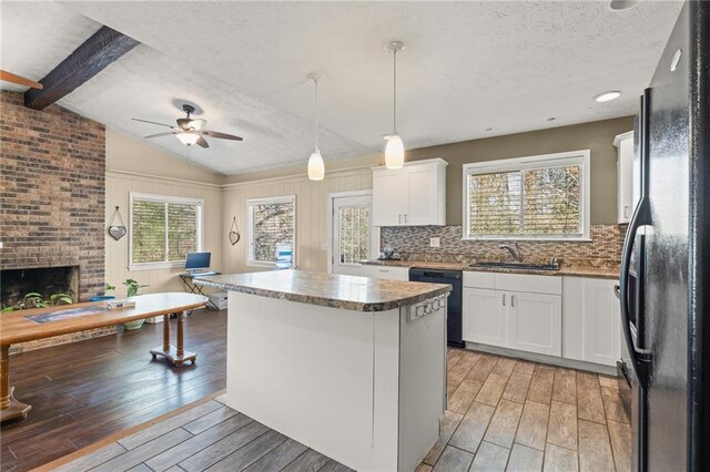 kitchen with sink, a brick fireplace, a kitchen island, white cabinets, and black appliances