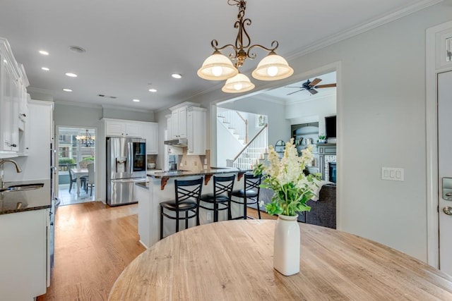 dining area with sink, ceiling fan with notable chandelier, ornamental molding, and light hardwood / wood-style floors