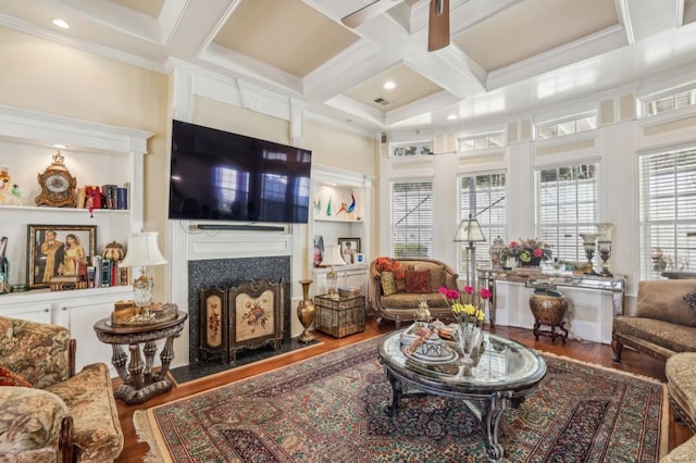 living area featuring coffered ceiling, wood finished floors, a fireplace, ornamental molding, and beam ceiling