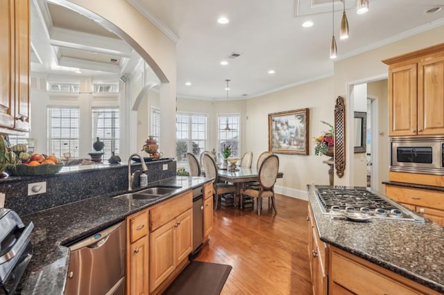 kitchen featuring dark stone counters, stainless steel appliances, a sink, and crown molding