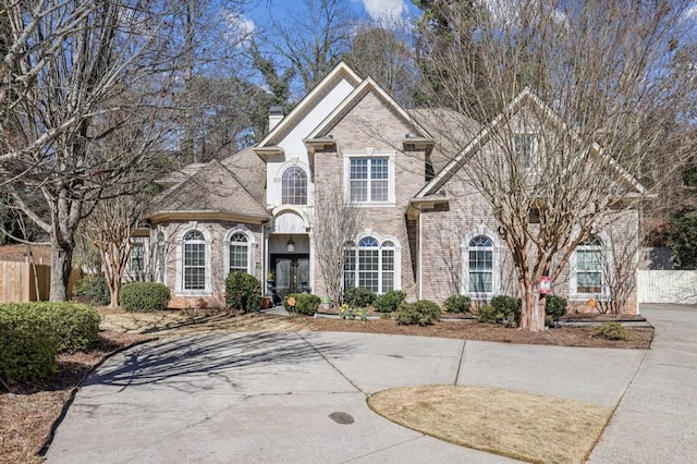 view of front of property with french doors, brick siding, a chimney, and fence