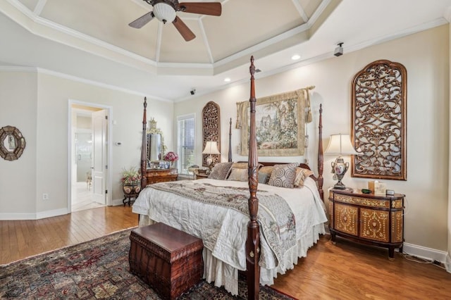 bedroom featuring wood finished floors, baseboards, a tray ceiling, ensuite bath, and crown molding