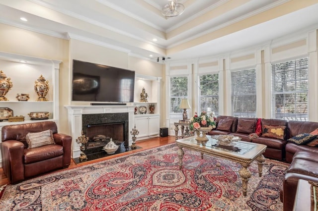 living area featuring a tray ceiling, ornamental molding, wood finished floors, and a high end fireplace