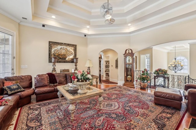 living room with arched walkways, a tray ceiling, wood finished floors, and ornamental molding