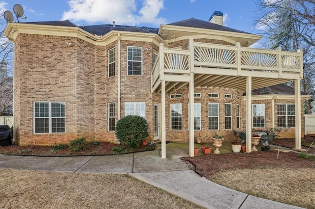 exterior space with a chimney, brick siding, a patio, and a deck