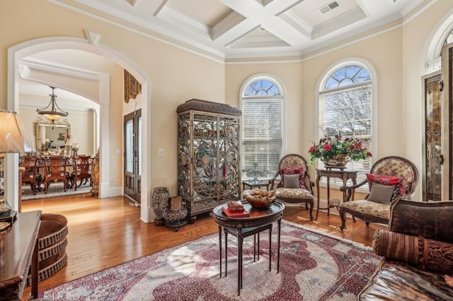 living area with arched walkways, coffered ceiling, wood finished floors, visible vents, and ornamental molding