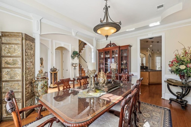 dining space with visible vents, arched walkways, wood finished floors, stairs, and crown molding