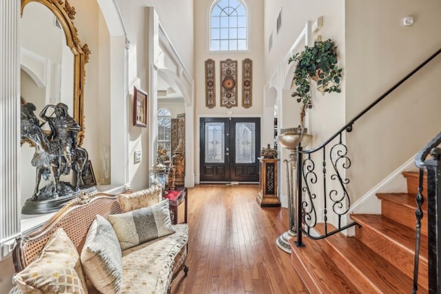 foyer featuring stairs, arched walkways, french doors, a towering ceiling, and hardwood / wood-style flooring