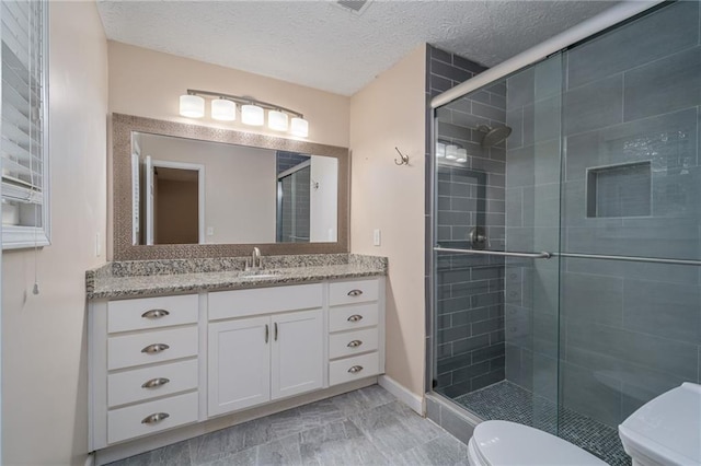 bathroom featuring a shower with door, vanity, a textured ceiling, and toilet