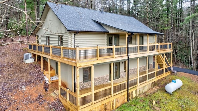 rear view of property featuring a shingled roof, cooling unit, a deck, and log siding