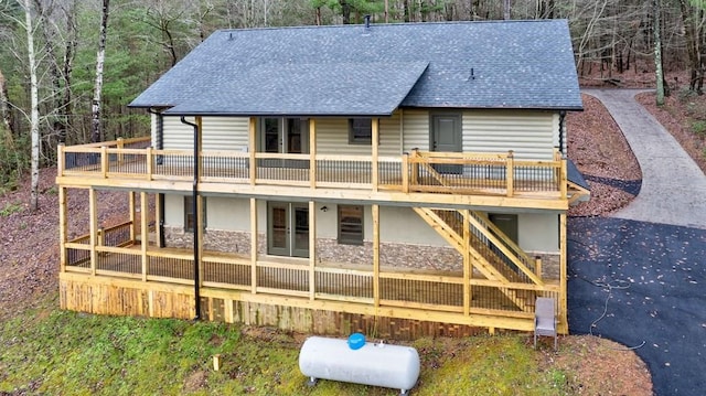 rear view of property with a deck, stone siding, french doors, stairway, and roof with shingles