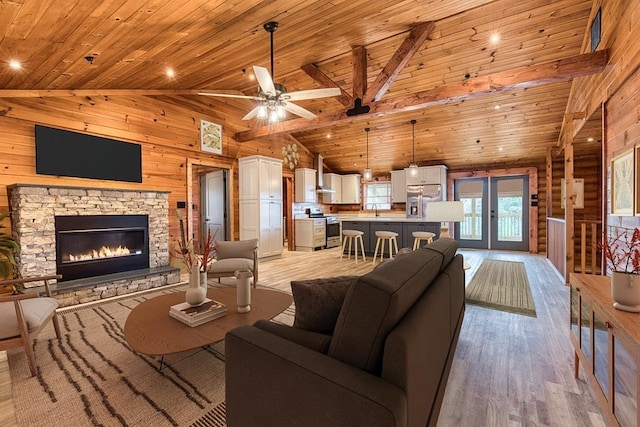 living area featuring high vaulted ceiling, a stone fireplace, wooden walls, wood ceiling, and light wood-type flooring