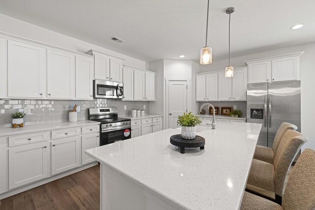 kitchen featuring visible vents, appliances with stainless steel finishes, white cabinetry, and a kitchen bar