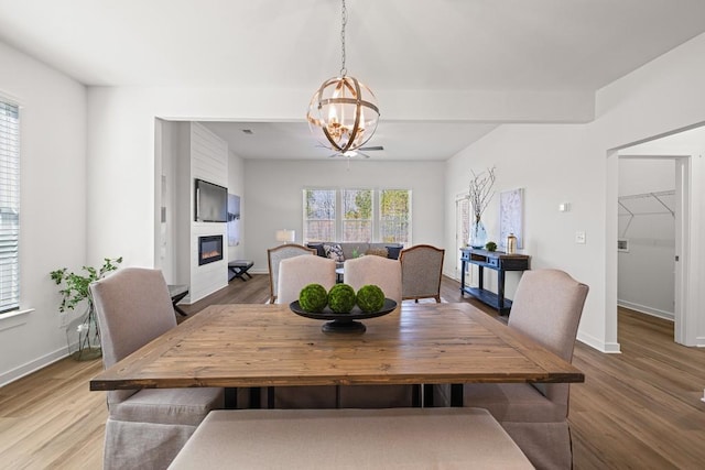 dining space featuring light wood-style flooring, a fireplace, baseboards, and a chandelier