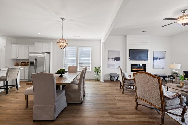 dining area featuring visible vents, a ceiling fan, a glass covered fireplace, baseboards, and dark wood-style flooring