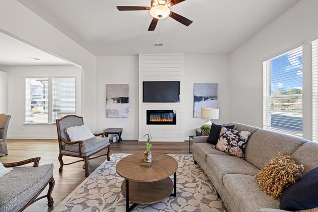 living room with a ceiling fan, plenty of natural light, wood finished floors, and a large fireplace