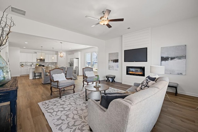 living area featuring visible vents, a ceiling fan, wood finished floors, a fireplace, and baseboards