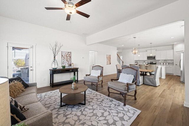 living room featuring stairs, baseboards, light wood-style flooring, and a ceiling fan