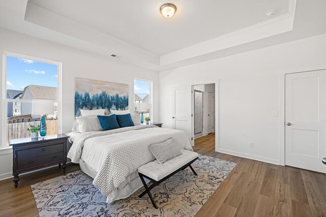 bedroom with visible vents, a raised ceiling, wood finished floors, crown molding, and baseboards