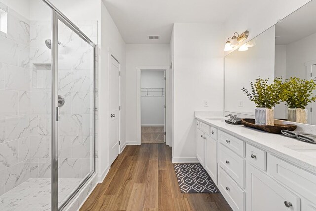 full bath featuring visible vents, a walk in closet, wood finished floors, a marble finish shower, and double vanity