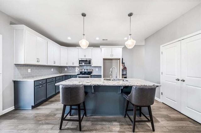 kitchen featuring stainless steel appliances, wood finished floors, a sink, white cabinetry, and tasteful backsplash